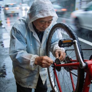 A candid street photo of an elderly Japanese man repairin...